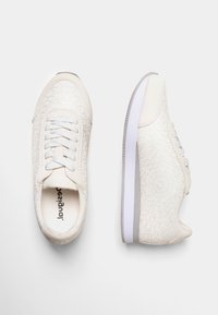 Zapatillas blancas con patrón floral texturizado, puntera redonda, cordones de color claro y suela blanca con un sutil acento gris a lo largo del borde.