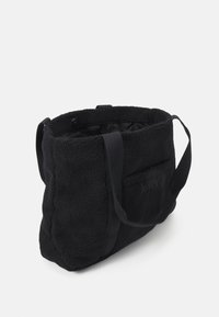 Černá taška přes rameno vyrobená z měkké, strukturované tkaniny, s uvolněným tvarem. Obsahuje pevné popruhy a zipový uzávěr, s jemným logem.