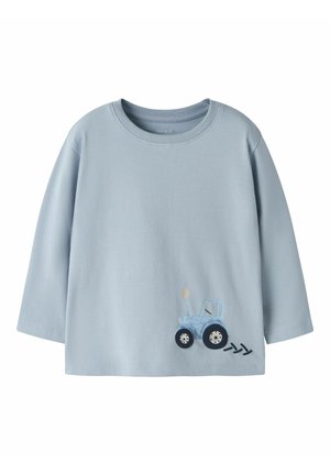 Jasnoniebieska koszulka z długim rękawem dla malucha z małym niebieskim traktorem i trzema czarnymi śladami opon blisko dolnego brzegu.