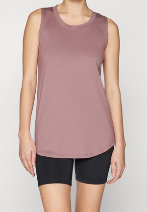 Personne portant un débardeur mauve sans manches et un short noir moulant sur un fond uni, bras détendus le long du corps.