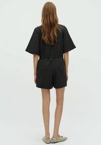 Giocomponibile nero a maniche corte con vita elasticizzata, tasche laterali e vestibilità comoda, abbinato a scarpe piatte a righe.