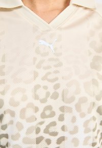 Beige idrottströja med ett subtilt leopardmönster, en v-ringad krage och en vit Puma-logotyp på vänster bröst.