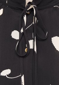 Blusa nera con motivi floreali bianchi astratti, modello con fiocco al collo e bottoni dorati. Realizzata in tessuto leggero e testurizzato.