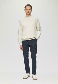 Lichtbeige sweatshirt, marineblau slim-fit broek, roomkleurige en bruine sneakers. Glad textuur, lange mouwen, minimalistisch ontwerp.