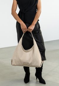Sac hobo en cuir beige au design décontracté et à la texture douce. Sangle en cuir et accent métallique subtil à l'avant. Convient pour une tenue décontractée.