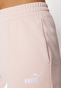 Rosa träningsbyxor med elastisk midja, sidofickor och vit broderad logotyp. Gjorda av mjukt tyg med en slät textur.