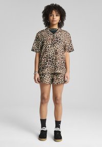 Conjunto de camisa de manga corta con estampado de leopardo y pantalones cortos en tonos beige y negro. Presenta un corte holgado, textura suave y un diseño de botón en la parte delantera.
