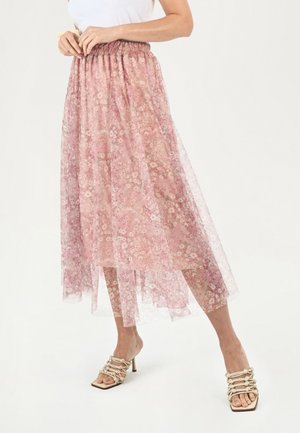 Jupe midi florale rose avec superposition transparente, taille élastique et design superposé. Portée avec des sandales à talons hauts beiges à lanières.