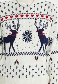 Stickad tröja med vit botten och mönster av marinblå och röda renar, hjärtan och snöflingor. Texturerad tyg med ribbade ärmslut och nederkant.