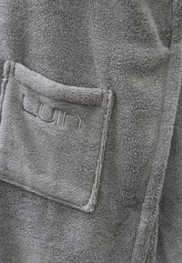 Accappatoio grigio in pile con tasca frontale e logo ricamato, dal tessuto morbido e soffice. Bottoni di chiusura visibili lungo il bordo.