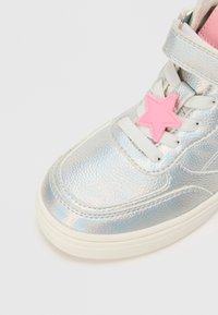 Hõbedased sünteetilised tossud läikiva, iridessentse viimistlusega, roosa tähekujuline aksessuaar, valged paelad ja kummist tald.