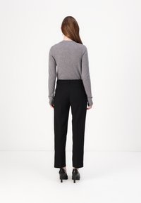 Grå uldtrøje og sorte skræddersyede bukser, der har en smal pasform og lige ben. Sorte hæle fuldender outfittet. Ingen synlige mønstre.