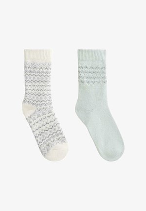 Weiße und mintgrüne Socken; der linke Socke hat ein Zickzackmuster in Grautönen, während die rechte Socke einfarbig mintgrün mit einer weichen Textur ist.