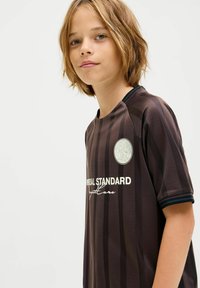 Camiseta de fútbol de manga corta a rayas marrones con escote redondo, que cuenta con un logotipo circular y texto blanco en la parte delantera, hecha de tela ligera.