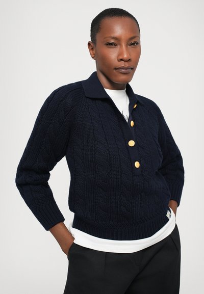 Pull en tricot bleu marine avec un motif en torsades, des poignets côtelés et un col. Il comporte quatre boutons dorés sur le devant. Coupe moderne.