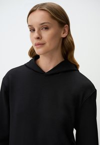 Czarna bluza z kapturem o luźnym kroju, z miękką fakturą i minimalnymi detalami szwów w okolicy dekoltu.