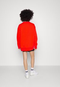 Roter, übergroßer Pullover mit langen Ärmeln, gerippten Bündchen und Saum. Getragen über einem gestreiften schwarzen Rock und kombiniert mit weißen Sneakers und Socken.
