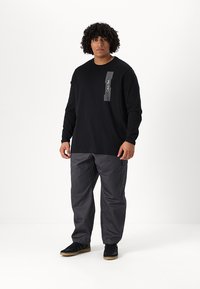 Black long-sleeve t-shirt with a vertical white striped graphic on the chest, paired with gray cargo pants and black sneakers.