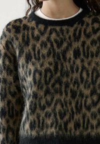 Svetri z vzorcem leoparda z črnimi in rjavimi puhastimi teksturami, temnim rebrastim dekoltejem in majhnim belim notranjim ovratnikom.