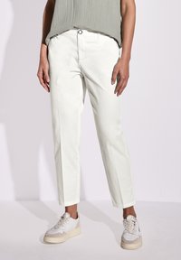 Pantaloni bianchi in cotone con un design a gamba dritta, dotati di chiusura con bottone frontale e tasche laterali, abbinati a sneaker di colore chiaro.