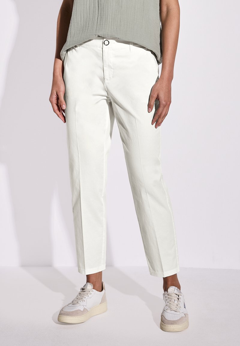 Pantaloni bianchi in cotone con un design a gamba dritta, dotati di chiusura con bottone frontale e tasche laterali, abbinati a sneaker di colore chiaro.