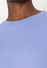 Felpa azzurro chiaro con collo a girocollo a coste, texture morbida e dettagli di cucitura visibili lungo il collo.