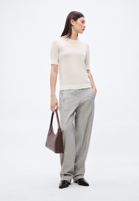 Jasnobeżowa krótka bluzka z dzianiny z krótkim rękawem w połączeniu z szarymi, taliowanymi spodniami, trzymająca ciemnobrązową skórzaną torebkę. Teksturowane dzianinowe detale na rękawach.
