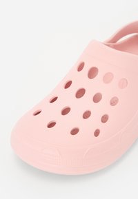 Light pink clogs with a rounded toe, made of flexible material. Features multiple ventilation holes and a textured edge for grip.