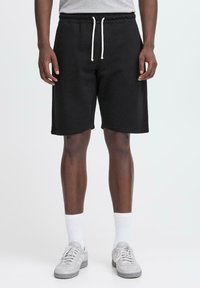 Pantalones cortos deportivos de algodón negro con cintura elástica y cordones blancos, con un corte holgado y sin patrones visibles.