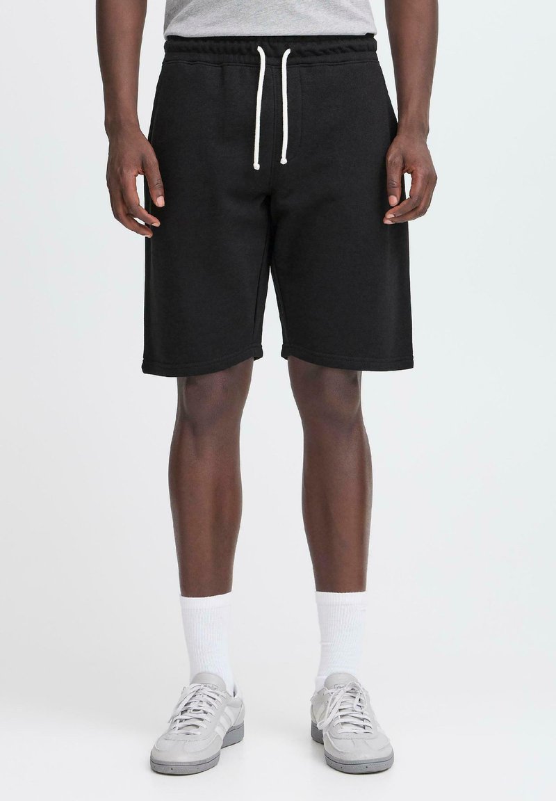 Pantalones cortos deportivos de algodón negro con cintura elástica y cordones blancos, con un corte holgado y sin patrones visibles.