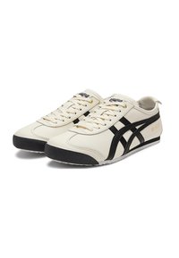 Cream-colored sneakers with black accents, smooth synthetic upper, lace-up design, and white sole with a textured black toe cap.