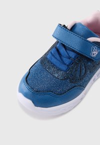 Adidaș albastru cu partea superioară sclipitoare, șireturi din material textil și o curea cu Velcro. Are un design cu fluture pe lateral și o talpă de cauciuc albă.