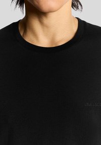 Sort crew-neck t-shirt lavet af glat bomuld, med et subtilt præget logo på brystområdet. Enkel og minimalistisk design.