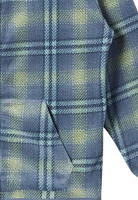 Sininen ja vihreä ruudullinen fleece-kangas, jossa on pehmeä tekstuuri, edessä tasku ja kontrastisia vaaleanvihreitä sekä tummansiniä viivoja.