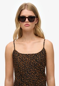 Gafas de sol con lentes oscuros y montura de carey. Accesorio que se lleva con una blusa sin mangas de estampado de leopardo marrón, con tirantes finos y escote cuadrado.
