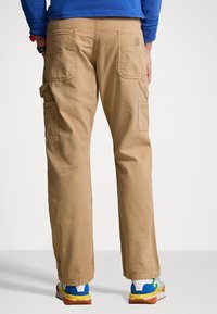 Khaki cargo-byxor med avslappnad passform, flera sidofickor och ett slitstarkt bomullsblandningsmaterial. Har-stickningar och förstärkta sömmar.