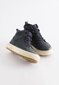 Sneakers alte in materiale grigio scuro con finitura testurizzata, suola in gomma beige, lacci e collo imbottito.