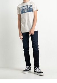 Camiseta gris claro con estampado gráfico azul, jeans ajustados oscuros, zapatillas negras y blancas con cordones. Diseño simple y apariencia casual.