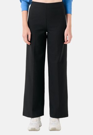 Zwarte wijde broek van een gladde, textiele stof, hoge taille en strakke lijnen, gecombineerd met witte sportschoenen.
