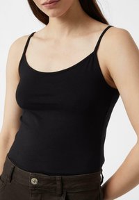 Czarny top na ramiączkach o cienkich paskach, wykonany z dopasowanego, elastycznego materiału. Posiada zaokrąglony dekolt i gładką teksturę. W zestawie z brązowymi spodniami.