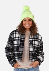 Black and white plaid jacket with a cropped design, paired with a light beige sweater. A bright green knitted beanie with a pom-pom completes the look.