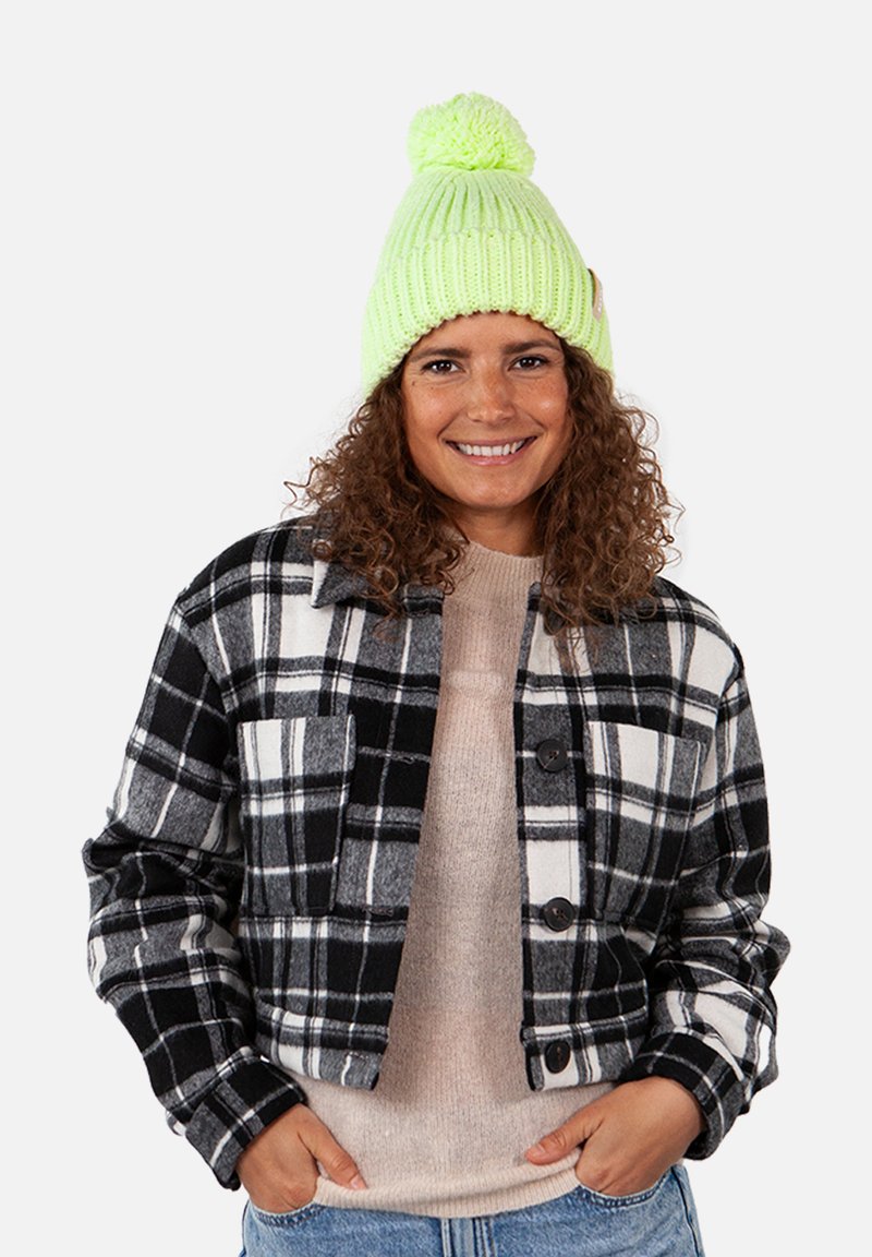 Black and white plaid jacket with a cropped design, paired with a light beige sweater. A bright green knitted beanie with a pom-pom completes the look.