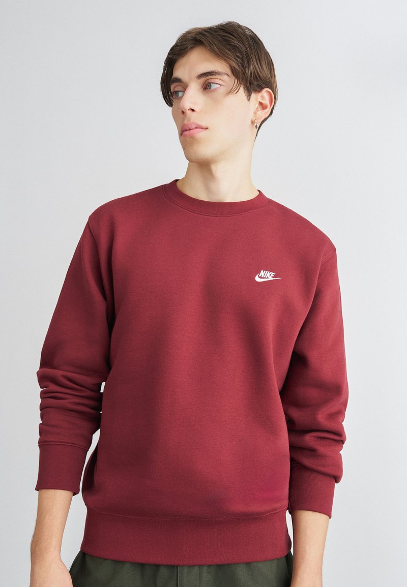 Bordový bavlnený sveter so stožkovými manžetami a golierom. Obsahuje malé biele logo Nike na hrudi, voľný strih. Mäkka textúra.