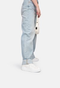 Hellblaue, hoch geschnittene Jeans mit aufgerolltem Saum, die am Kn�öchel mit einem goldenen Akzent versehen sind. Kombiniert mit weißen Sneakers und einer kleinen weißen Tasche.