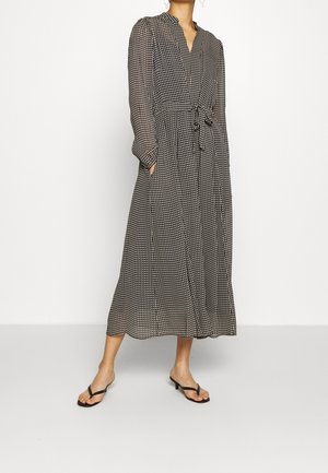 Mujer con vestido midi de manga larga con estampado en negro y blanco con cinturón anudado, combinado con sandalias negras de tacón.