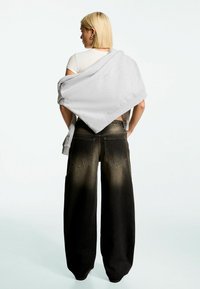 Grey sweatshirt loosely draped over a white shirt, paired with wide-leg, faded black jeans featuring two back pockets.