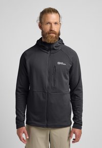 Veste noire zippée avec capuche, en tissu texturé, et logo blanc contrastant sur la poitrine gauche. Dotée d'une poche latérale zippée.