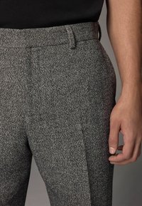 Szare spodnie w wzory z teksturowanej tkaniny, z płaskim przodem, paskami i slim fit, pokazane obok ręki spoczywającej na materiale.