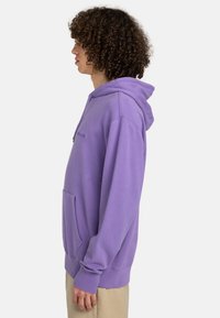Lila hoodie med en framficka, ribbade ärmslut och dragsko i huvan. Tillverkad av mjukt tyg med en avslappnad passform och minimal logotyp.