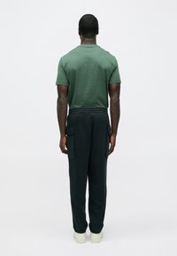 Zöld rövid ujjú pamut póló, sötét cargo nadrággal oldal zsebekkel és rugalmas szegélyekkel, világos tornacipővel viselve.